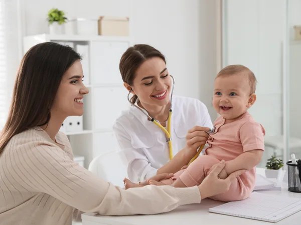 Pediatra auscultando a una bebé sonriente junto a su madre en la consulta