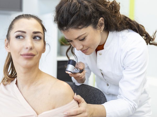 Dermatóloga revisando con dermatoscopio la piel del hombro de una paciente