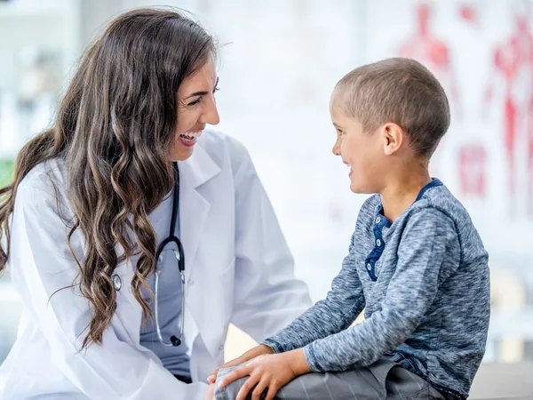 Doctora conversando sonriente con un niño en edad escolar durante una consulta