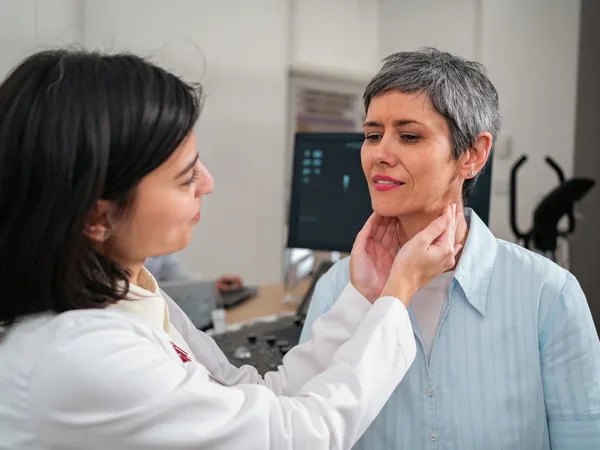 Doctora palpando la tiroides en el cuello de una paciente adulta